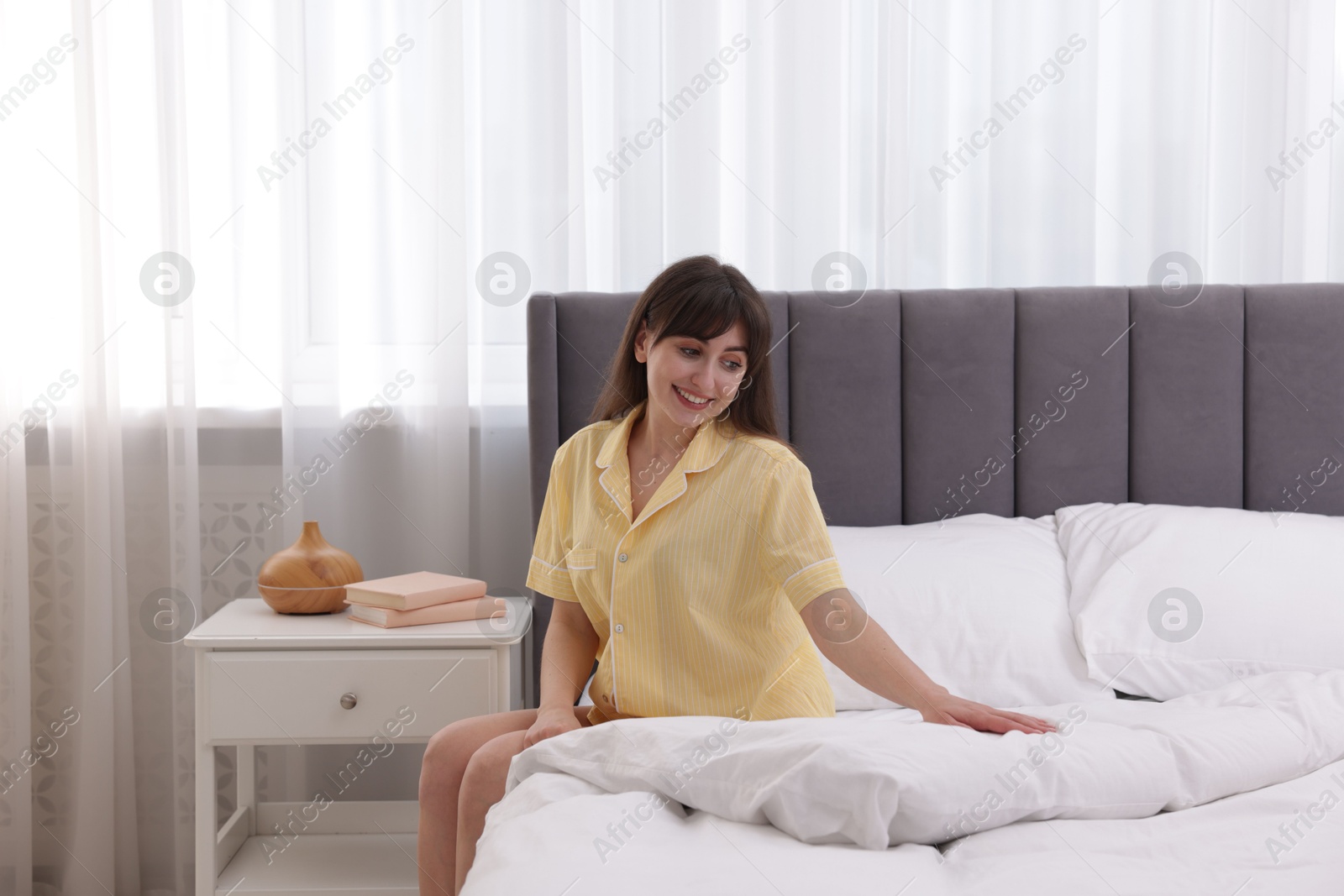 Beautiful young woman sitting on bed at home Photo of Beautiful young woman sitting on bed at home