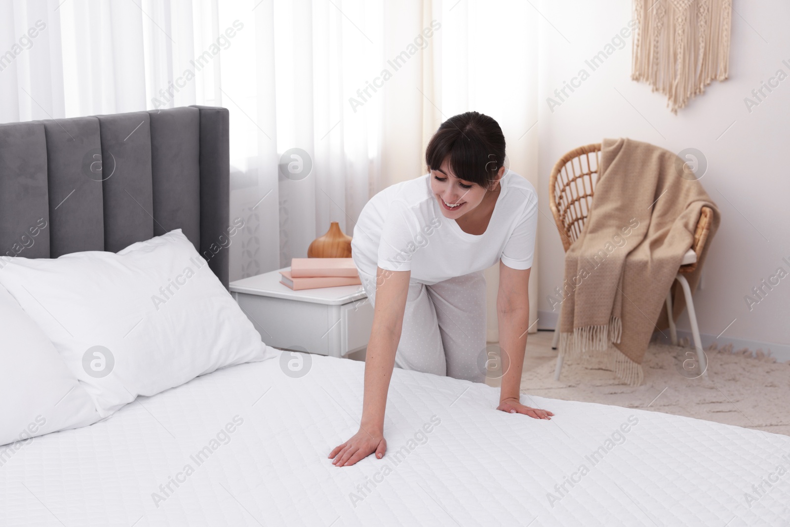 Beautiful woman putting cover on soft mattress at home Photo of Beautiful woman putting cover on soft mattress at home