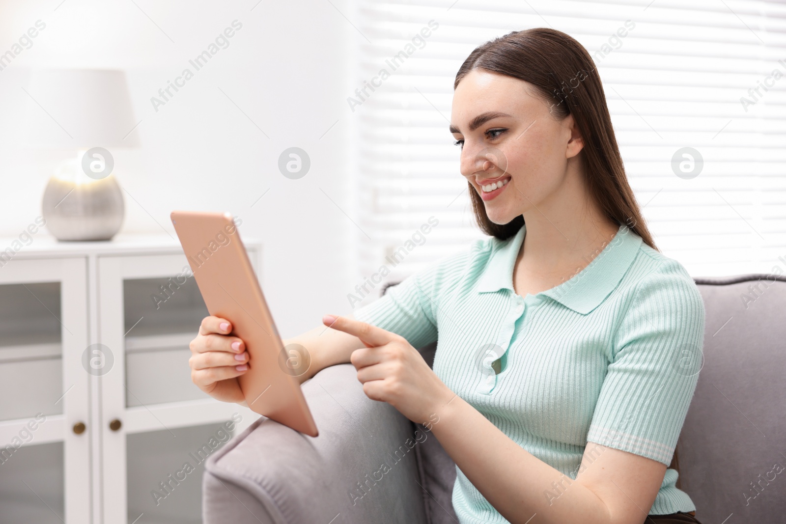 Young woman using modern tablet in armchair at home Photo of Young woman using modern tablet in armchair at home