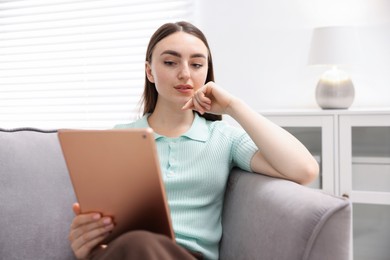 Photo of Young woman using modern tablet in armchair at home