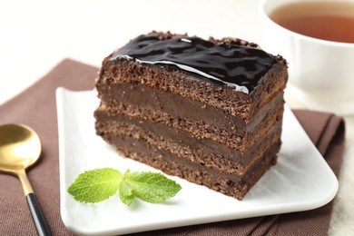 Photo of Piece of chocolate cake served with mint and spoon on table, closeup