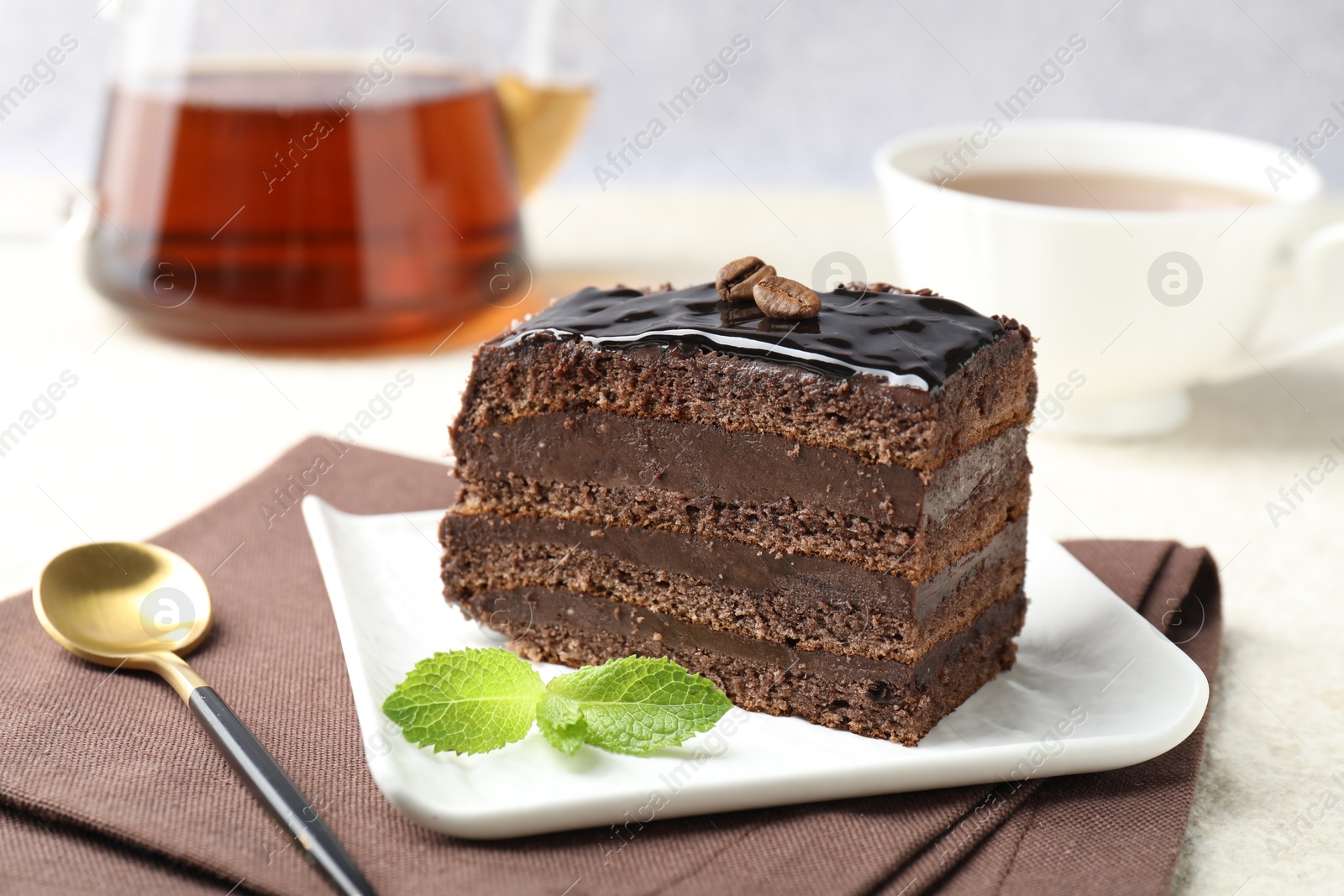 Photo of Piece of chocolate cake served with mint, spoon and tea on white table, closeup