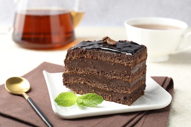 Photo of Piece of chocolate cake served with mint, spoon and tea on white table, closeup
