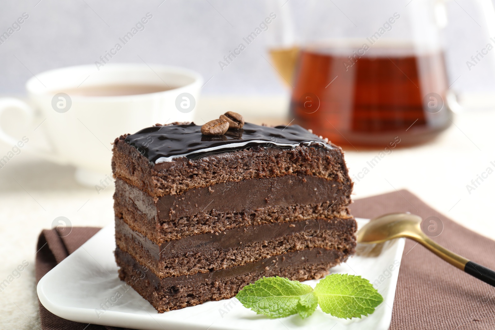Photo of Piece of chocolate cake served with mint, spoon and tea on table, closeup