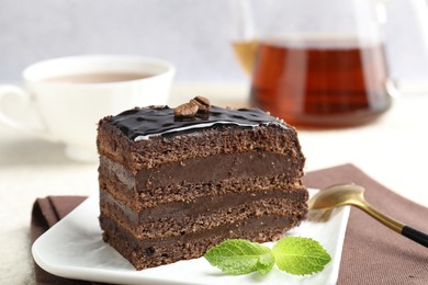 Photo of Piece of chocolate cake served with mint, spoon and tea on table, closeup
