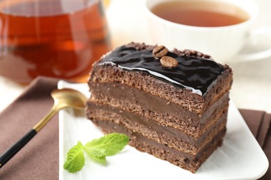 Photo of Piece of chocolate cake served with mint, spoon and tea on table, closeup