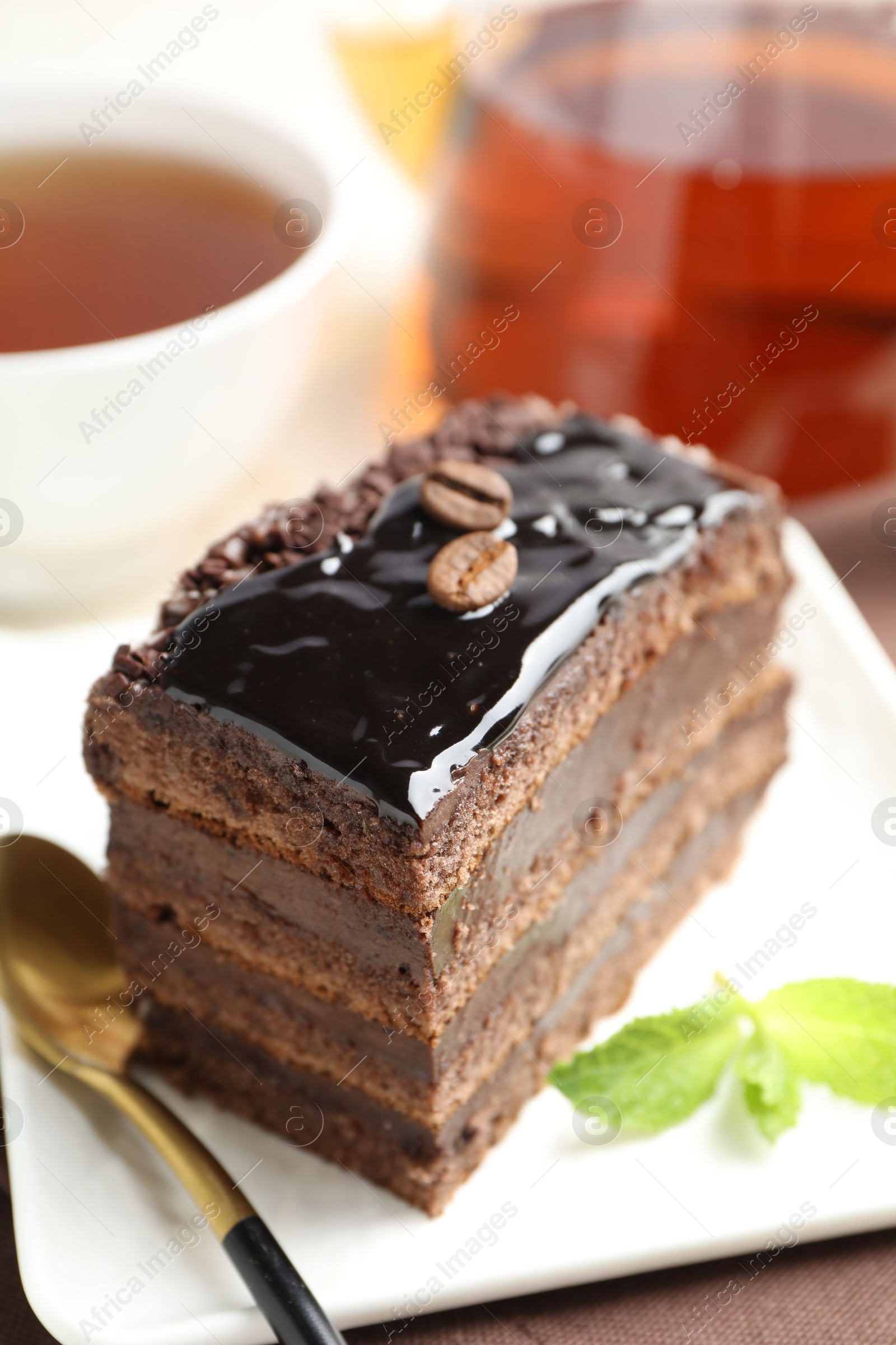 Photo of Piece of chocolate cake served with mint, spoon and tea on table, closeup