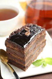 Photo of Piece of chocolate cake served with mint, spoon and tea on table, closeup