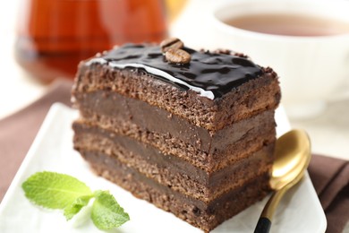 Photo of Piece of chocolate cake served with mint, spoon and tea on table, closeup