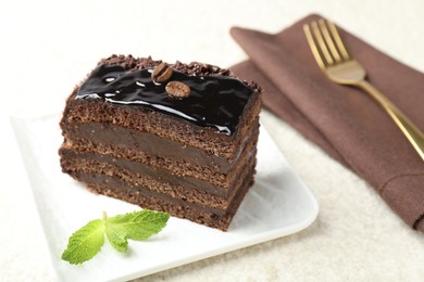 Photo of Piece of chocolate cake served with mint and fork on white table, closeup