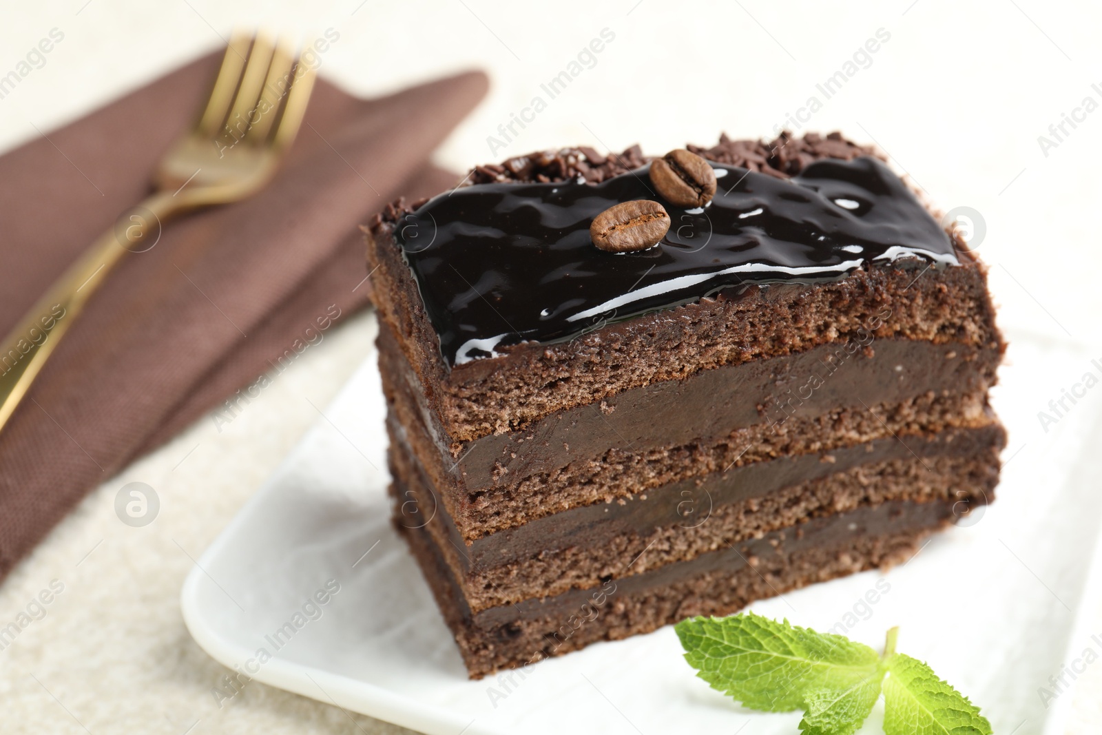 Photo of Piece of chocolate cake served with mint and fork on white table, closeup