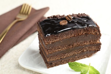 Photo of Piece of chocolate cake served with mint and fork on white table, closeup