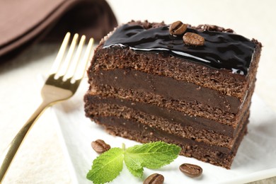 Photo of Piece of chocolate cake served with mint and fork on white table, closeup