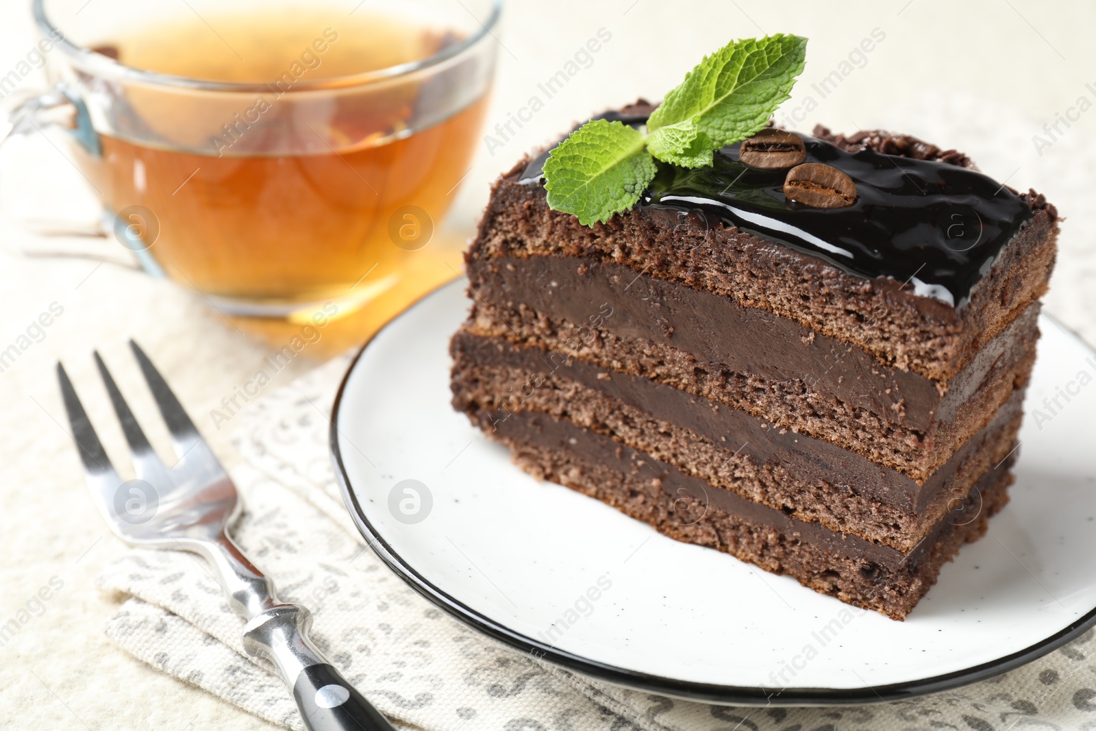 Photo of Piece of chocolate cake served with mint, fork and tea on table, closeup