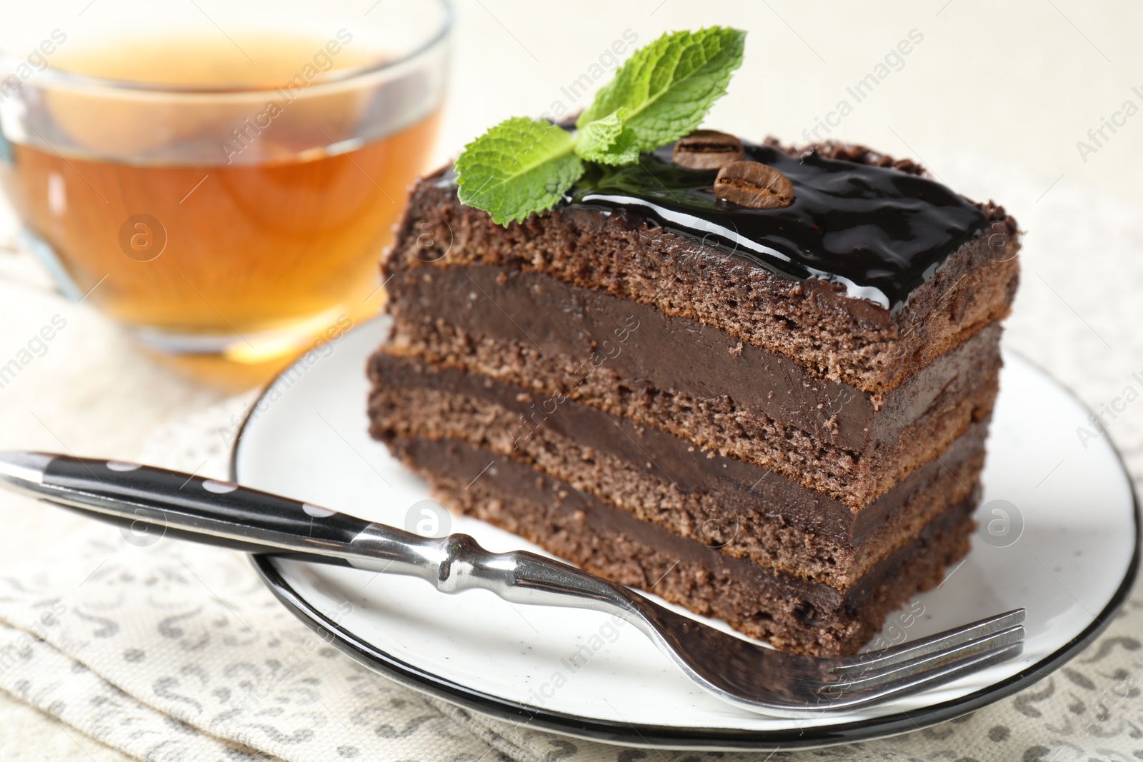 Photo of Piece of chocolate cake served with mint, fork and tea on table, closeup