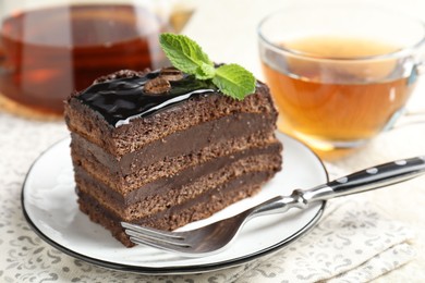 Photo of Piece of chocolate cake served with mint, fork and tea on table, closeup