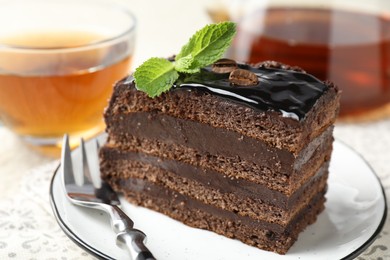 Photo of Piece of chocolate cake served with mint, fork and tea on table, closeup