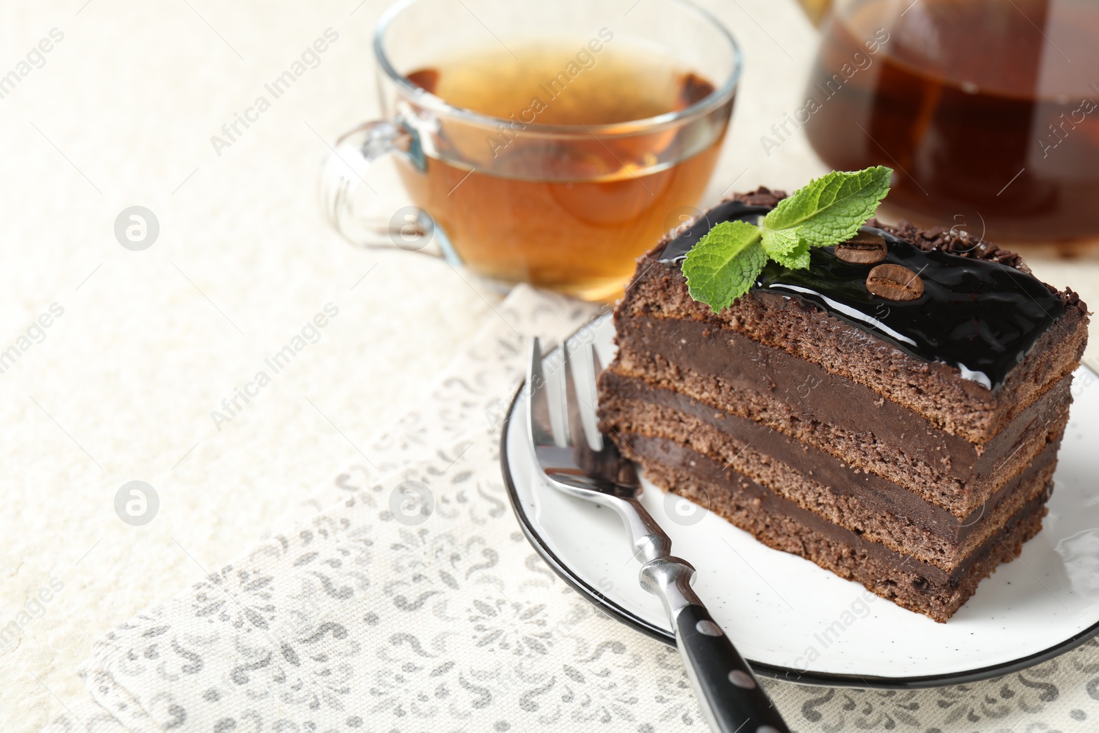 Photo of Piece of chocolate cake served with mint, fork and tea on white table, closeup. Space for text