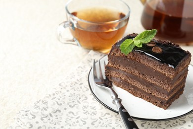 Photo of Piece of chocolate cake served with mint, fork and tea on white table, closeup. Space for text