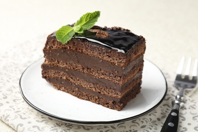 Photo of Piece of chocolate cake served with mint and fork on table, closeup