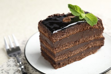 Photo of Piece of chocolate cake served with mint and fork on table, closeup