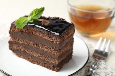Photo of Piece of chocolate cake served with mint, fork and tea on table, closeup