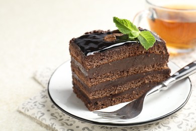 Photo of Piece of chocolate cake served with mint, fork and tea on white table, closeup