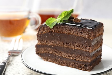 Photo of Piece of chocolate cake served with mint, fork and tea on table, closeup