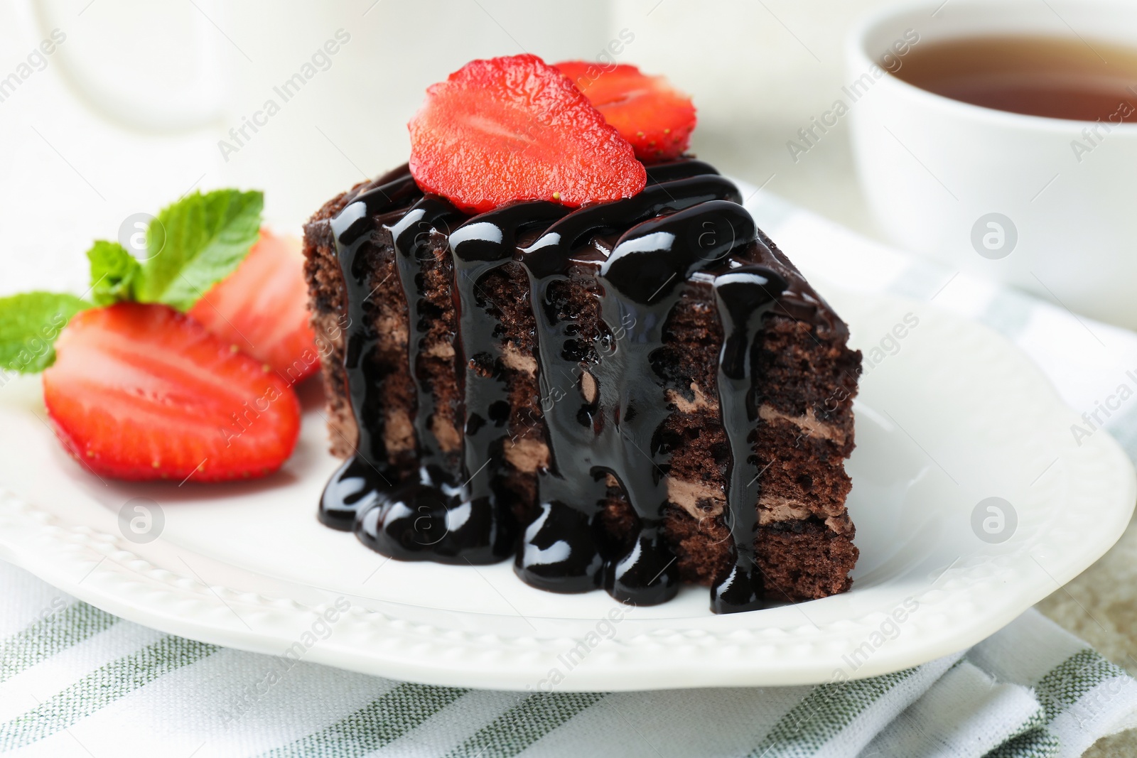 Photo of Piece of chocolate cake served with strawberries and tea on table, closeup