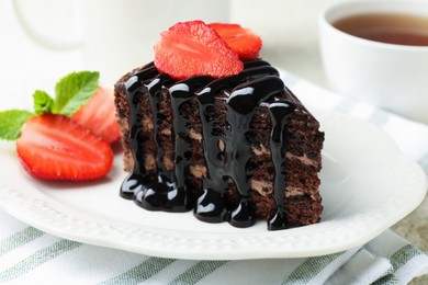 Photo of Piece of chocolate cake served with strawberries and tea on table, closeup