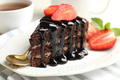 Photo of Piece of chocolate cake served with strawberries, spoon and tea on table, closeup