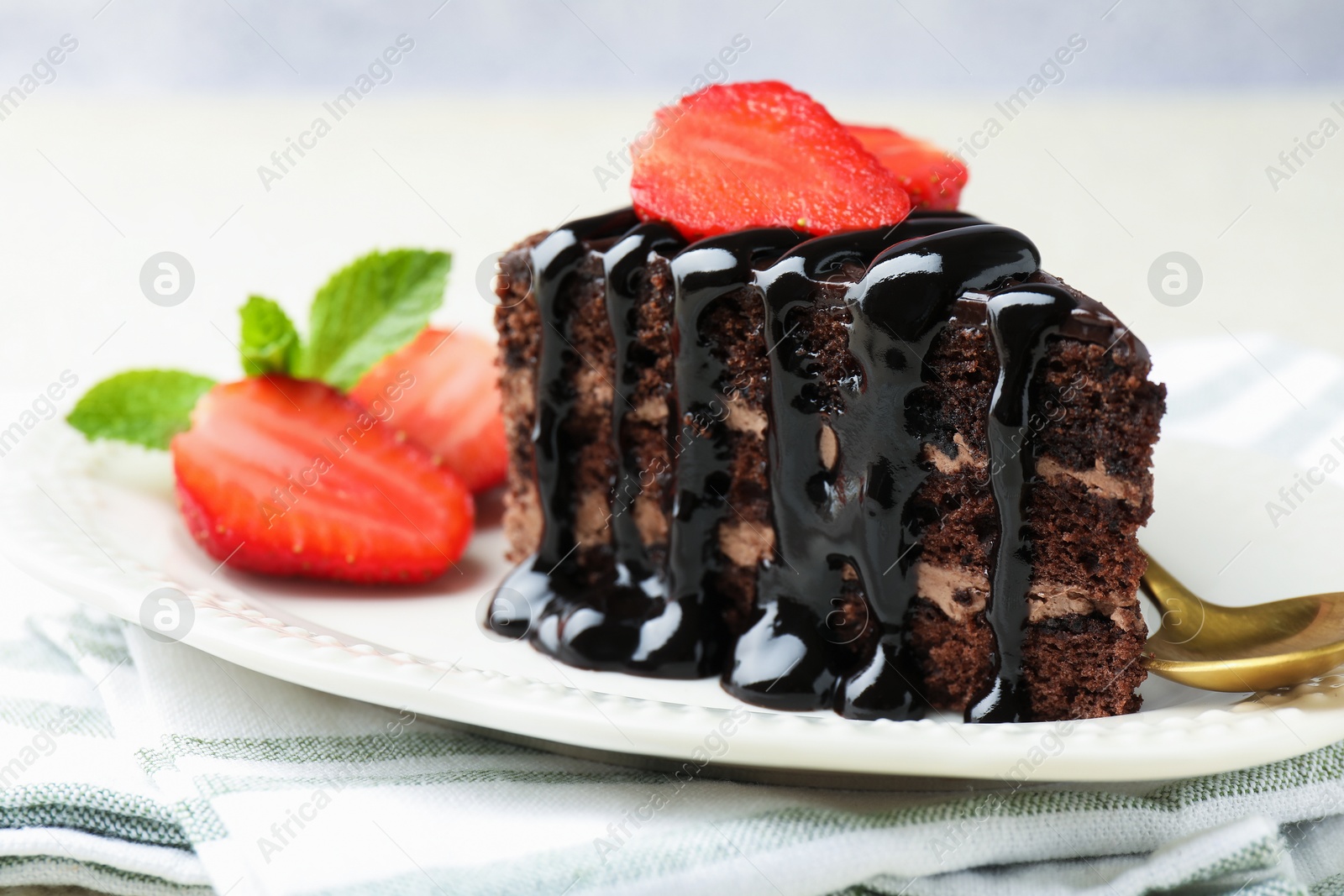 Photo of Piece of chocolate cake served with strawberries and spoon on table, closeup