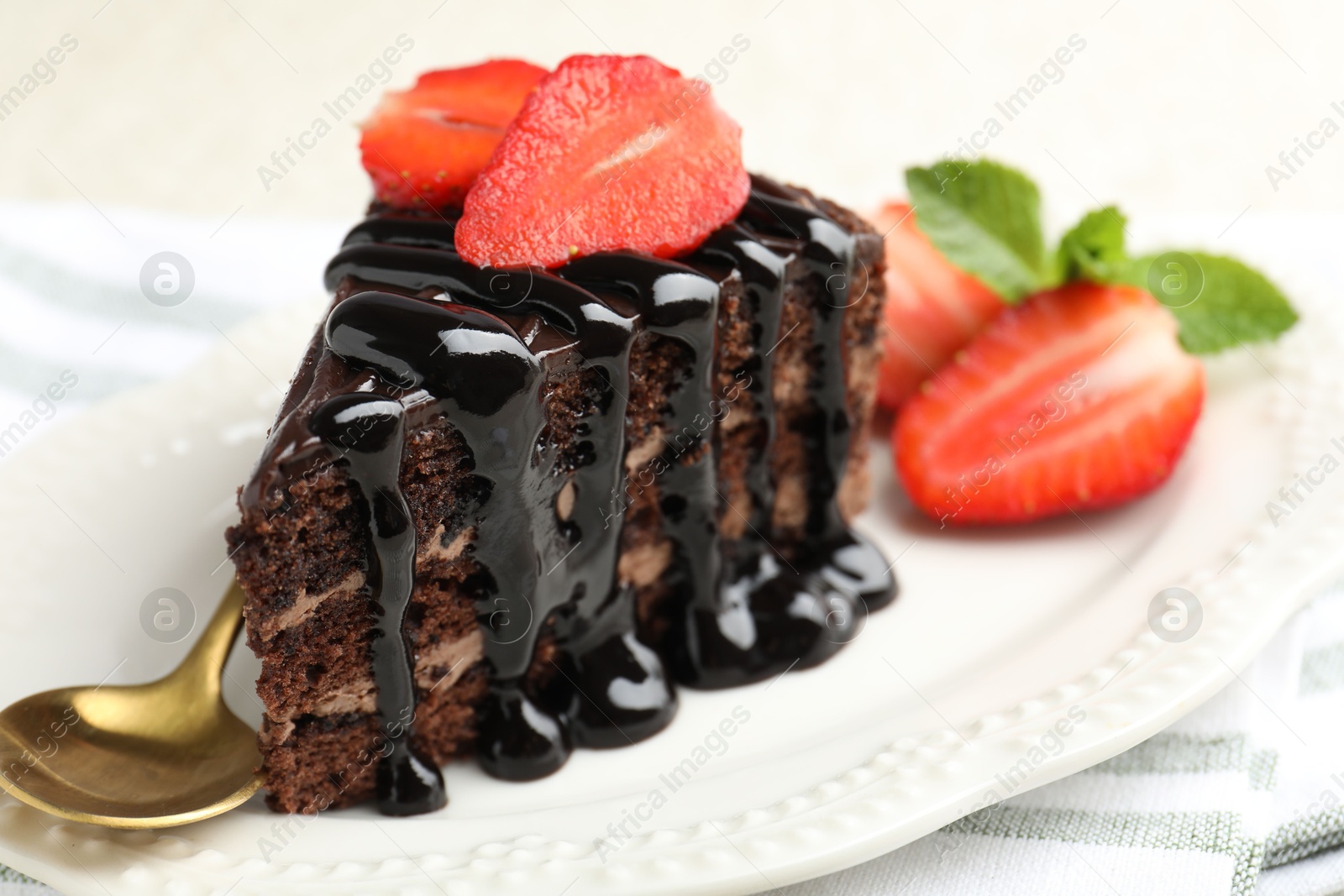 Photo of Piece of chocolate cake served with strawberries and spoon on table, closeup