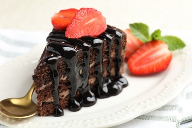 Photo of Piece of chocolate cake served with strawberries and spoon on table, closeup