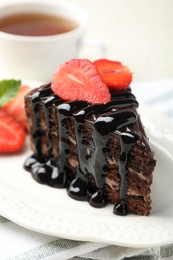 Photo of Piece of chocolate cake served with strawberries and tea on table, closeup