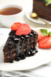 Photo of Piece of chocolate cake served with strawberries and tea on table, closeup