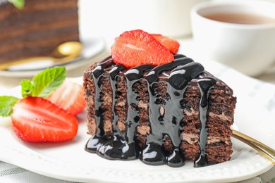 Photo of Piece of chocolate cake served with strawberries and tea on table, closeup