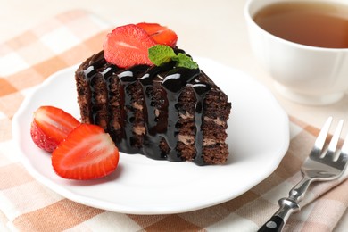 Photo of Piece of chocolate cake served with strawberries, tea and fork on table, closeup