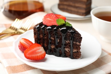 Photo of Piece of chocolate cake served with strawberries and tea on table, closeup