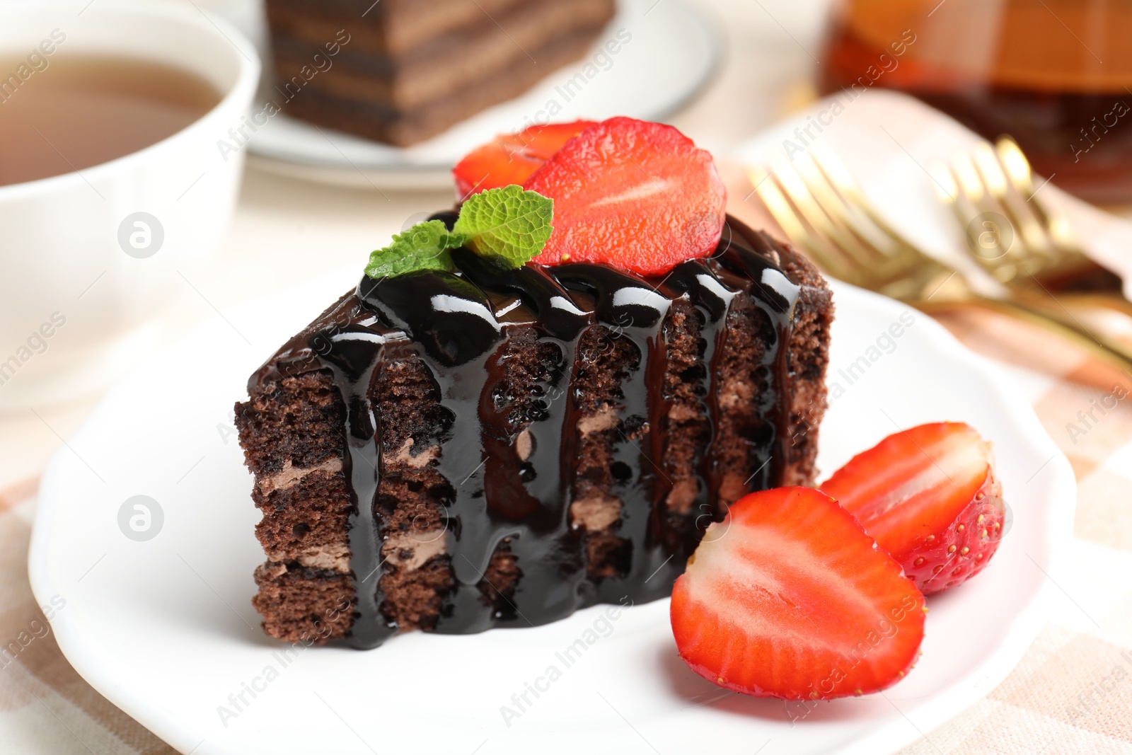 Photo of Piece of chocolate cake served with strawberries and tea on table, closeup