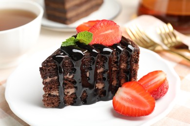 Photo of Piece of chocolate cake served with strawberries and tea on table, closeup