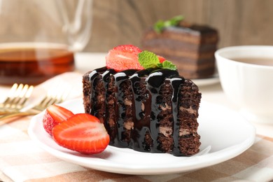 Photo of Piece of chocolate cake served with strawberries and tea on table, closeup