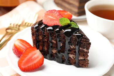 Photo of Piece of chocolate cake served with strawberries and tea on table, closeup