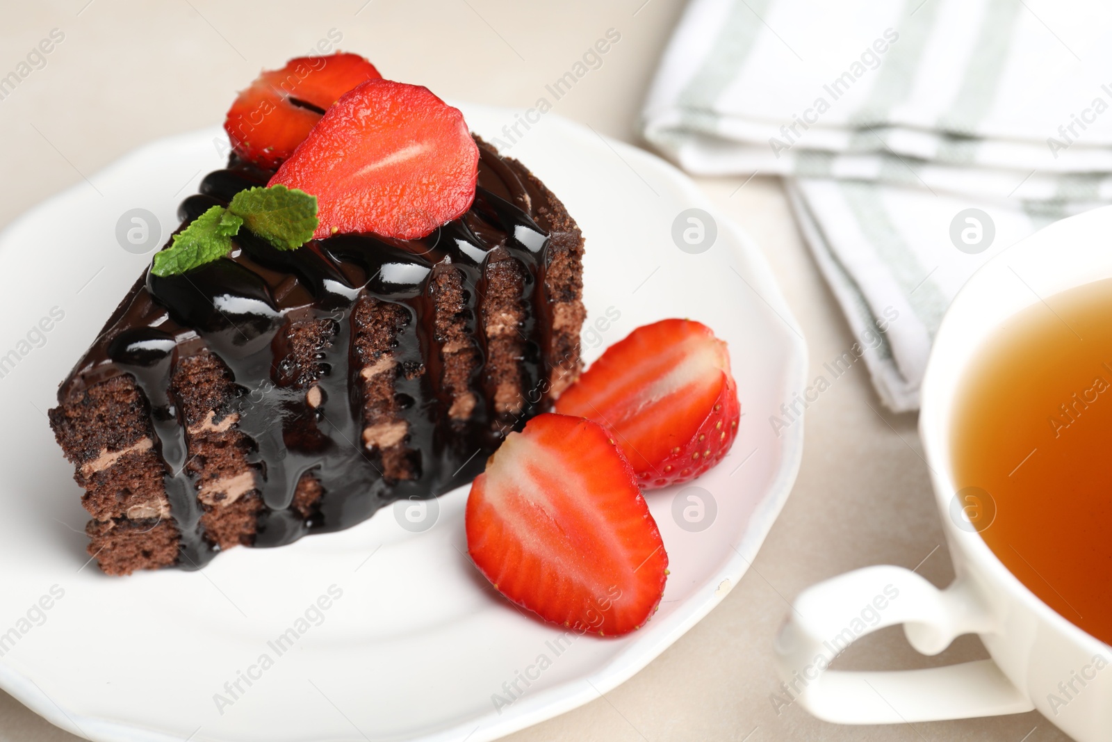 Photo of Piece of chocolate cake served with strawberries and tea on white table, closeup
