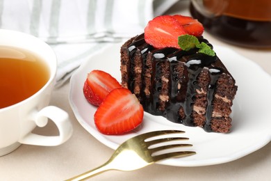 Photo of Piece of chocolate cake served with strawberries, tea and fork on white table, closeup