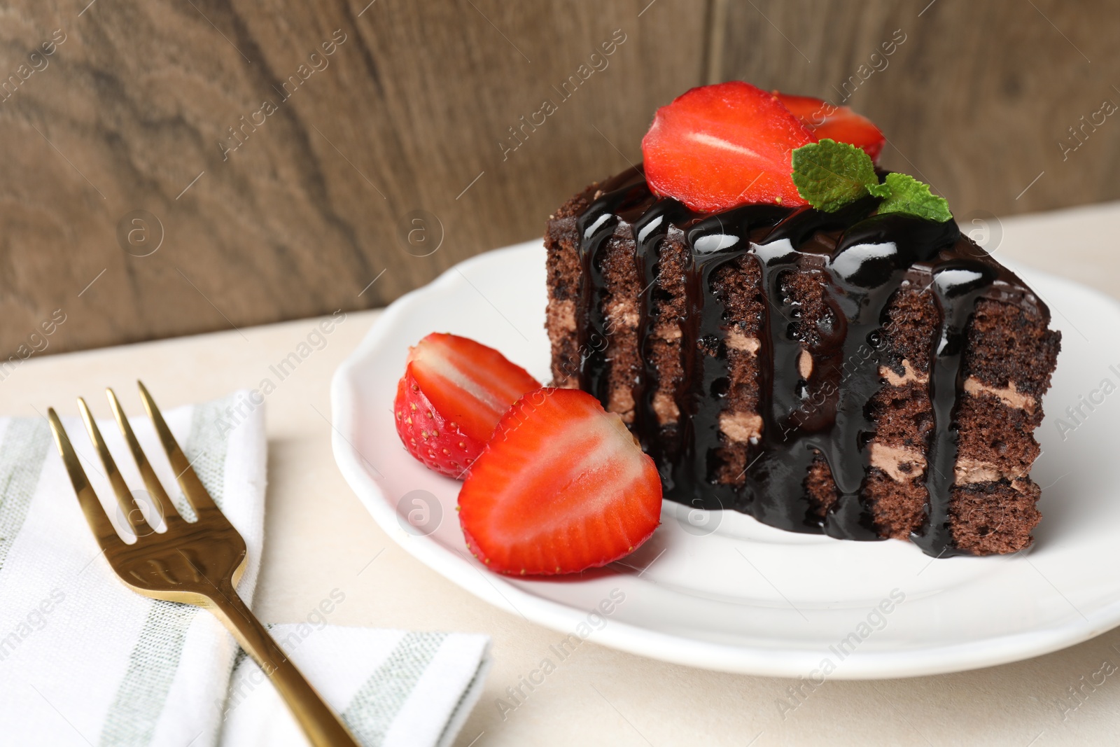 Photo of Piece of chocolate cake served with strawberries and fork on white table, closeup