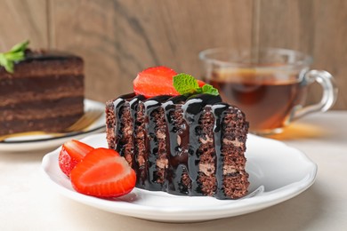 Photo of Piece of chocolate cake served with strawberries and tea on white table, closeup