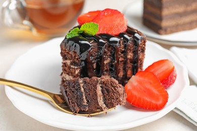 Photo of Piece of chocolate cake served with strawberries and spoon on white table, closeup