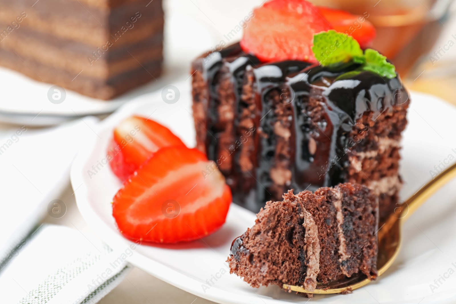 Piece of chocolate cake served with strawberries and spoon on white table, closeup Photo of Piece of chocolate cake served with strawberries and spoon on white table, closeup