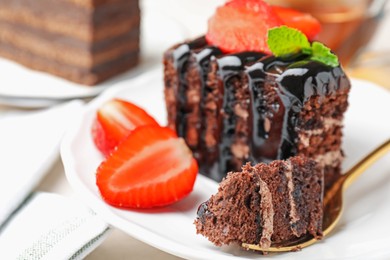 Photo of Piece of chocolate cake served with strawberries and spoon on white table, closeup